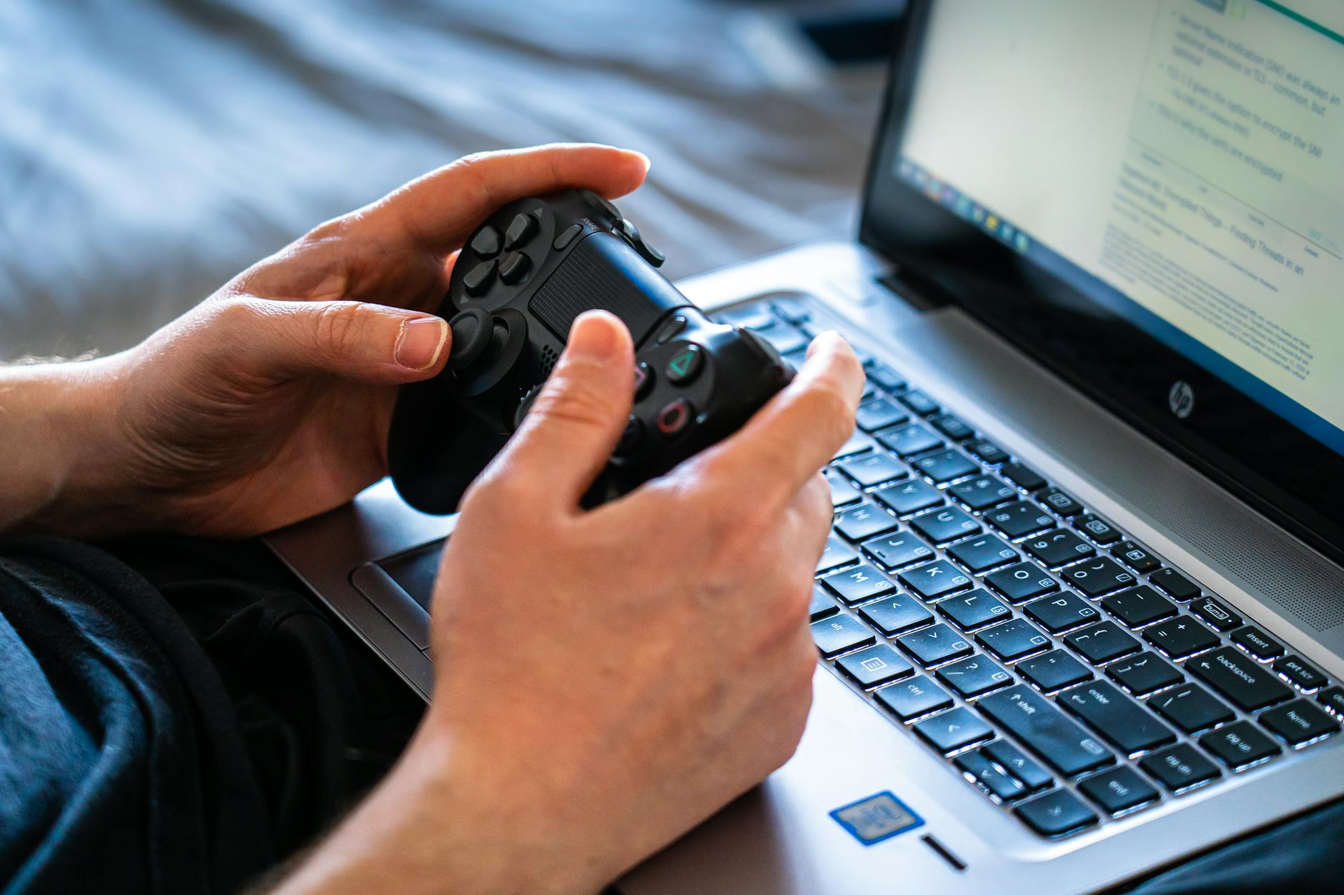Person using laptop for gaming with wireless controller on desk